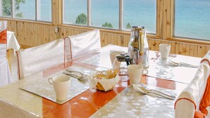 Un coin repas avec une table dressée pour deux personnes, une vue sur la mer grâce à de grandes fenêtres et des lambris en bois sur les murs.
