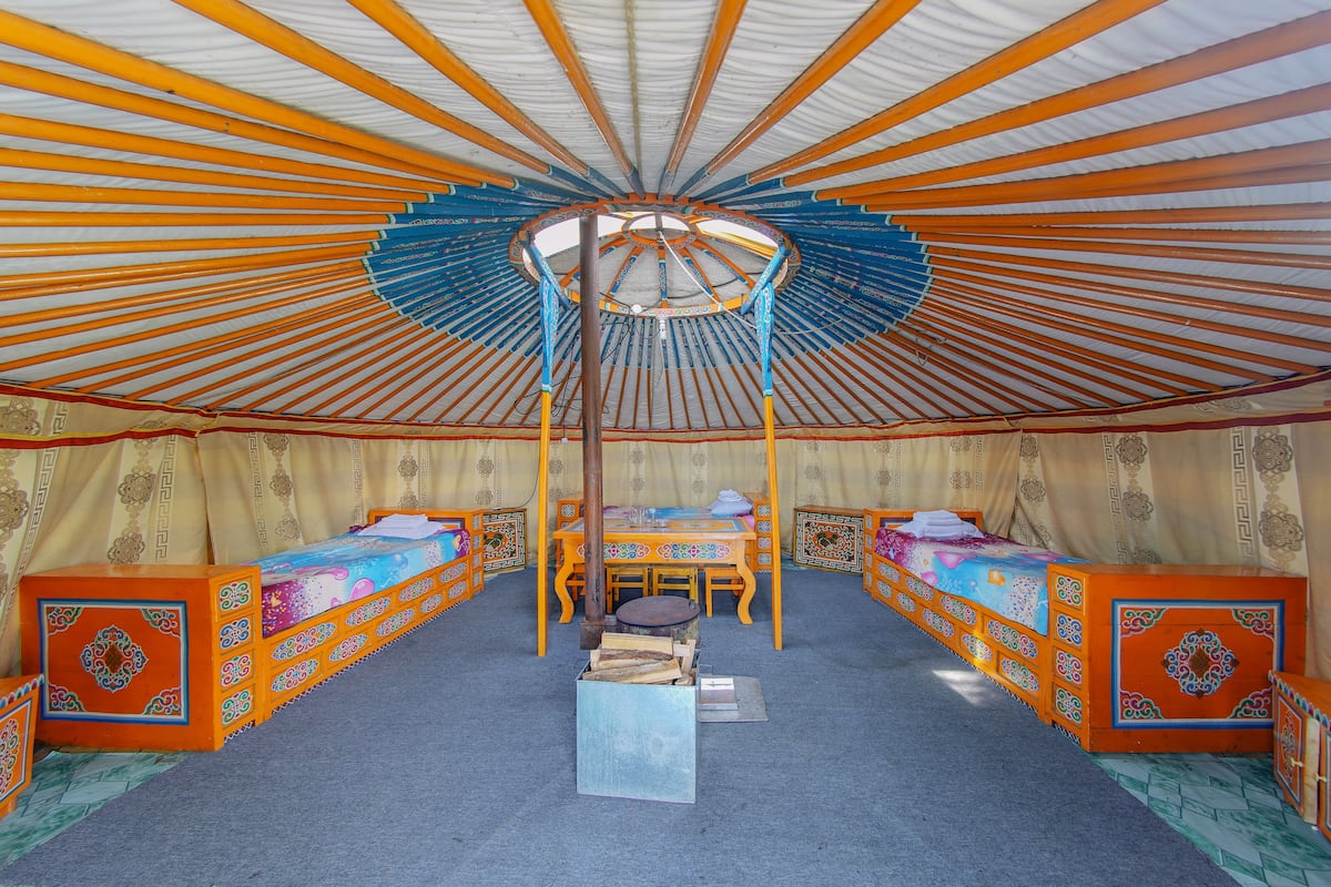 Une yourte traditionnelle avec un poteau central en bois, deux lits avec une literie colorée, une table et une chaise.