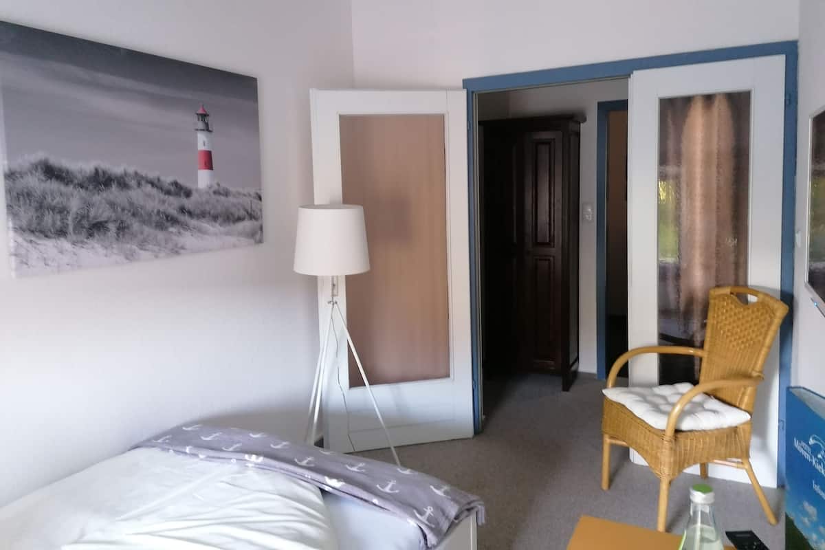 A hotel room with a bed, a chair, a lamp, a painting, and a door leading to another room.