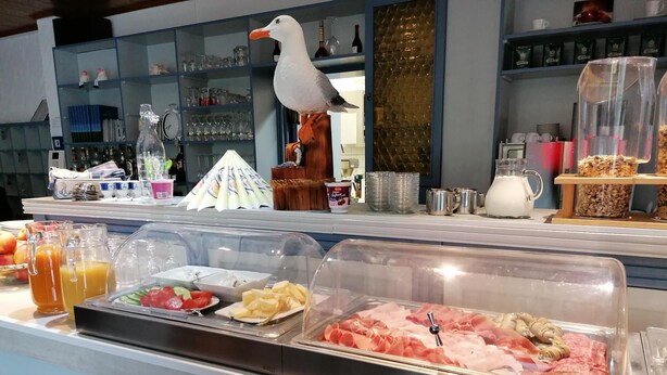 A buffet area with various food items, including fruits, salads, and meats, and a decorative seagull statue. - Frühstückshotel Möven Kieker (Friedrichskoog)