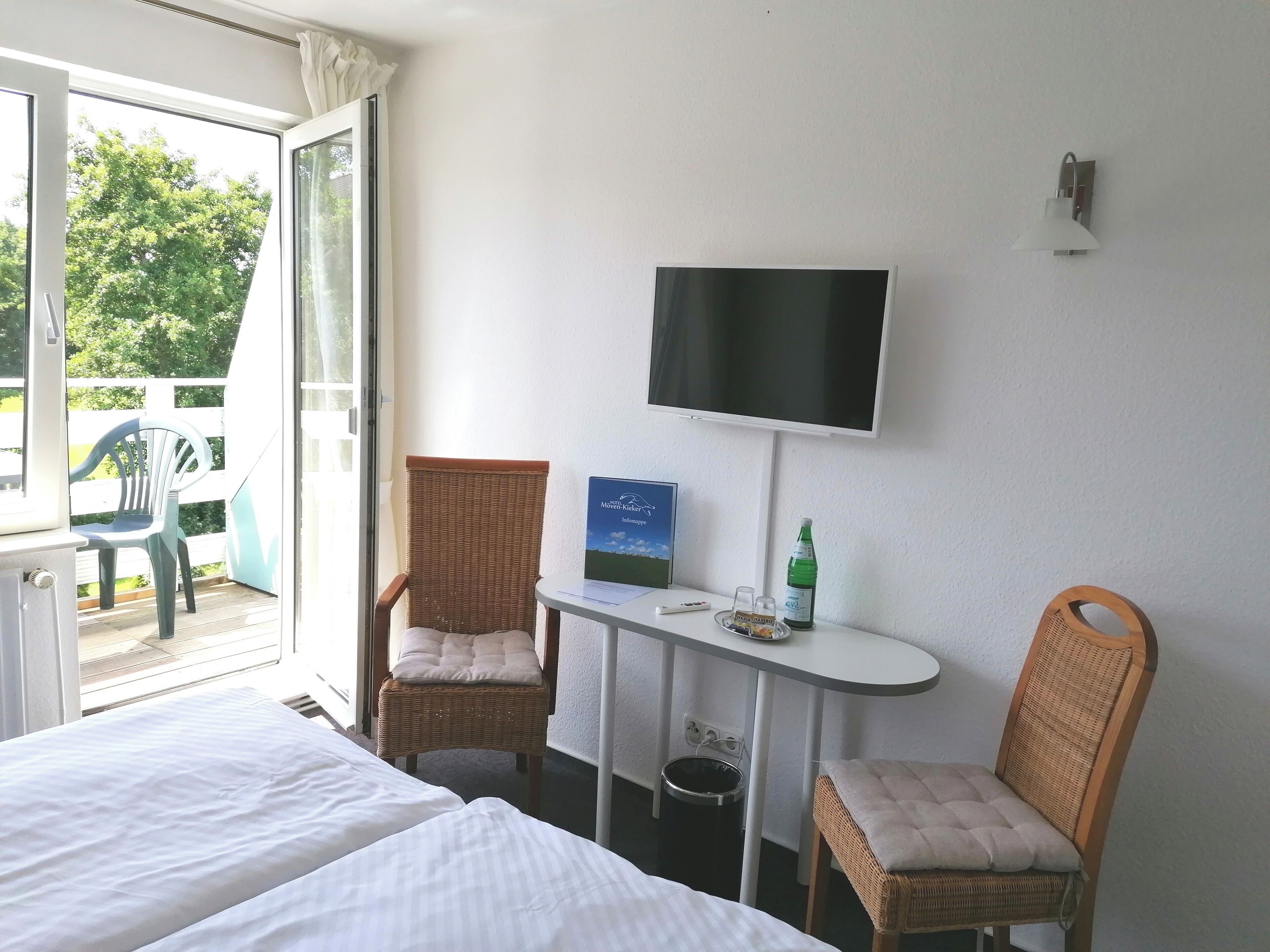 Een hotelkamer met een bed, een stoel, een klein tafeltje met een televisie, een fles en een prullenbak.