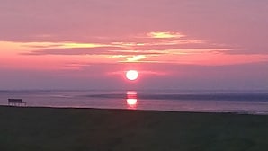 A sunset over a beach with a bench and calm water. - Frühstückshotel Möven Kieker (Friedrichskoog)