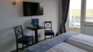 A hotel room with a bed, a TV mounted on the wall, a small table with a bottle and glasses, two chairs, and a window with curtains. - Frühstückshotel Möven Kieker (Friedrichskoog)