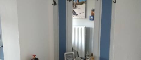 A small room with a white and blue vanity, a fire extinguisher, and a mirror with a painting above it.