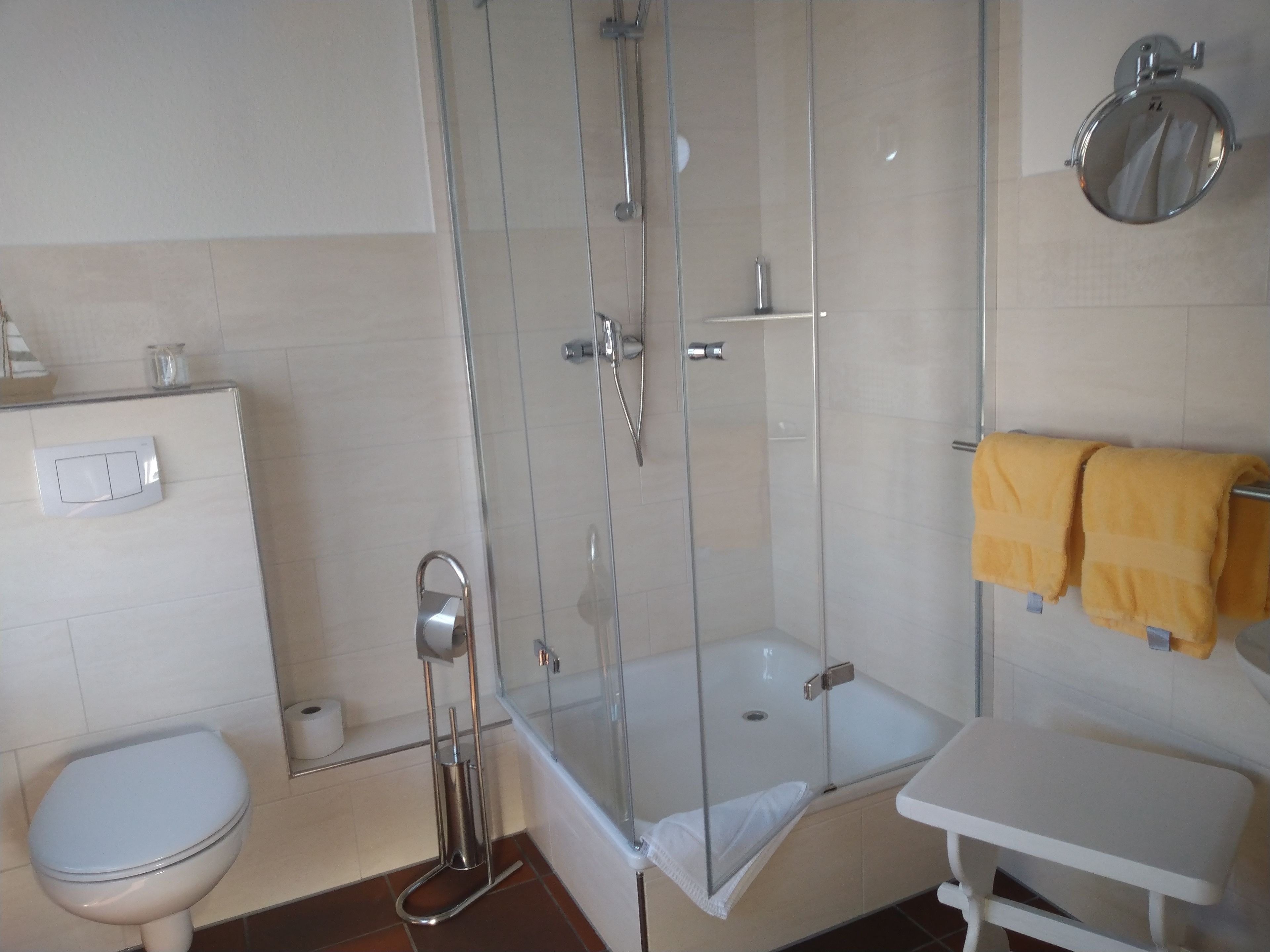 A bathroom with a glass-enclosed shower, a toilet, a sink, and a towel rack with a yellow towel.