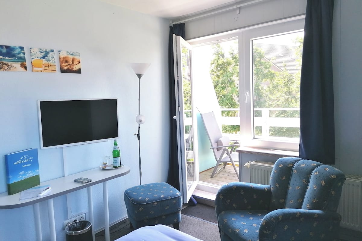 A hotel room with a bed, a desk with a flat-screen TV, a chair, a small table, and a window with a view of the outside.
