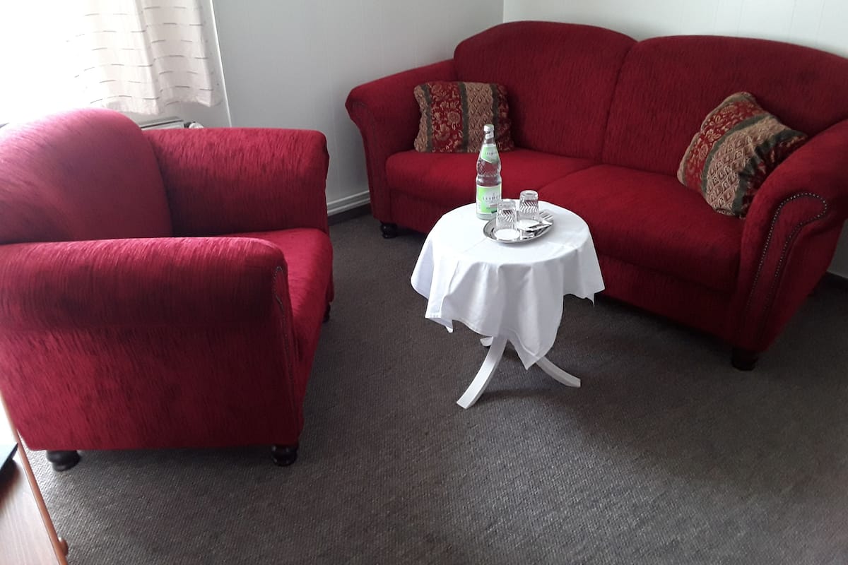 A red armchair and sofa set with a small table in between, a bottle of water, and salt and pepper shakers on the table.