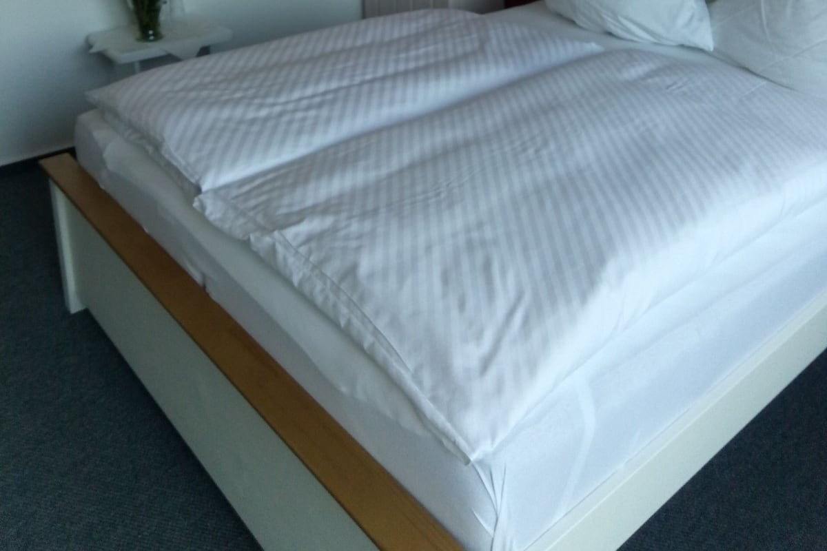A neatly made bed with white linens, a white wardrobe, and a wall with a lighthouse decal.