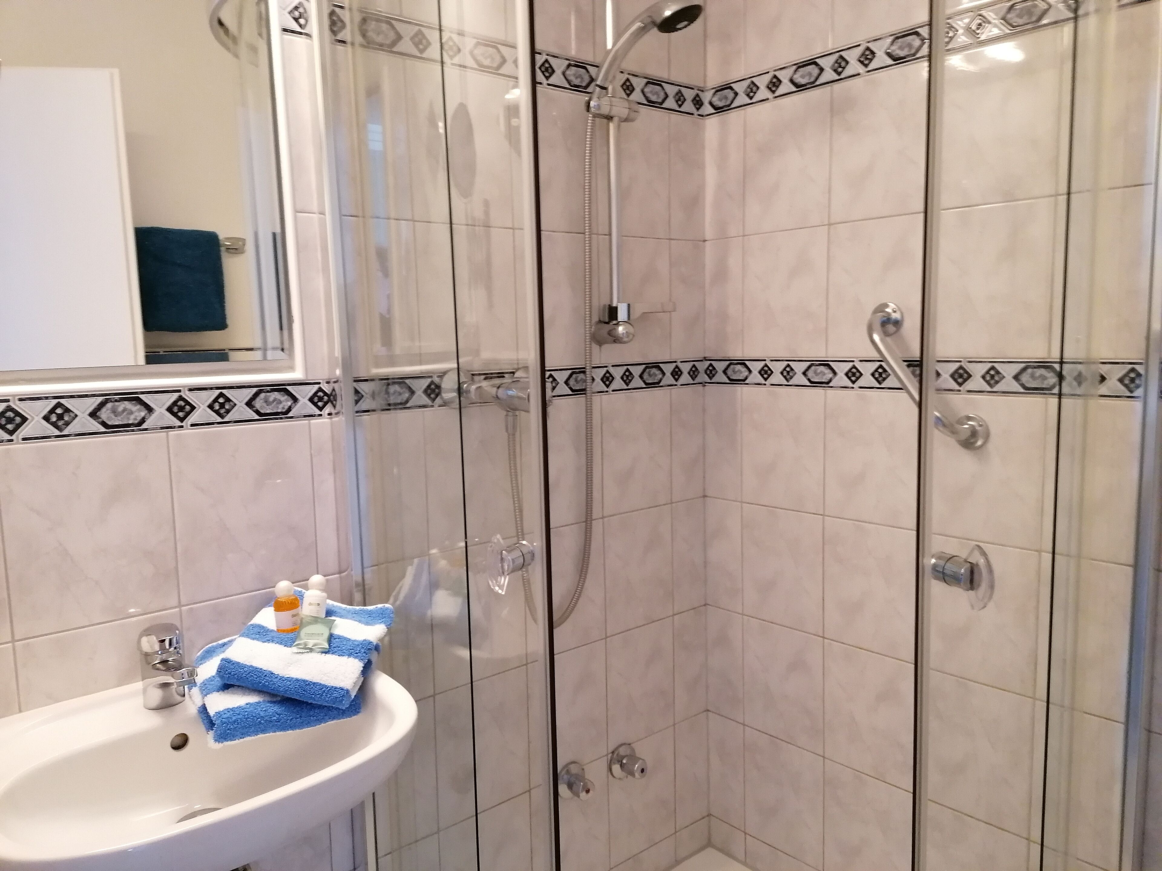 A bathroom with a shower, a sink with a blue and white striped towel, and toiletries.