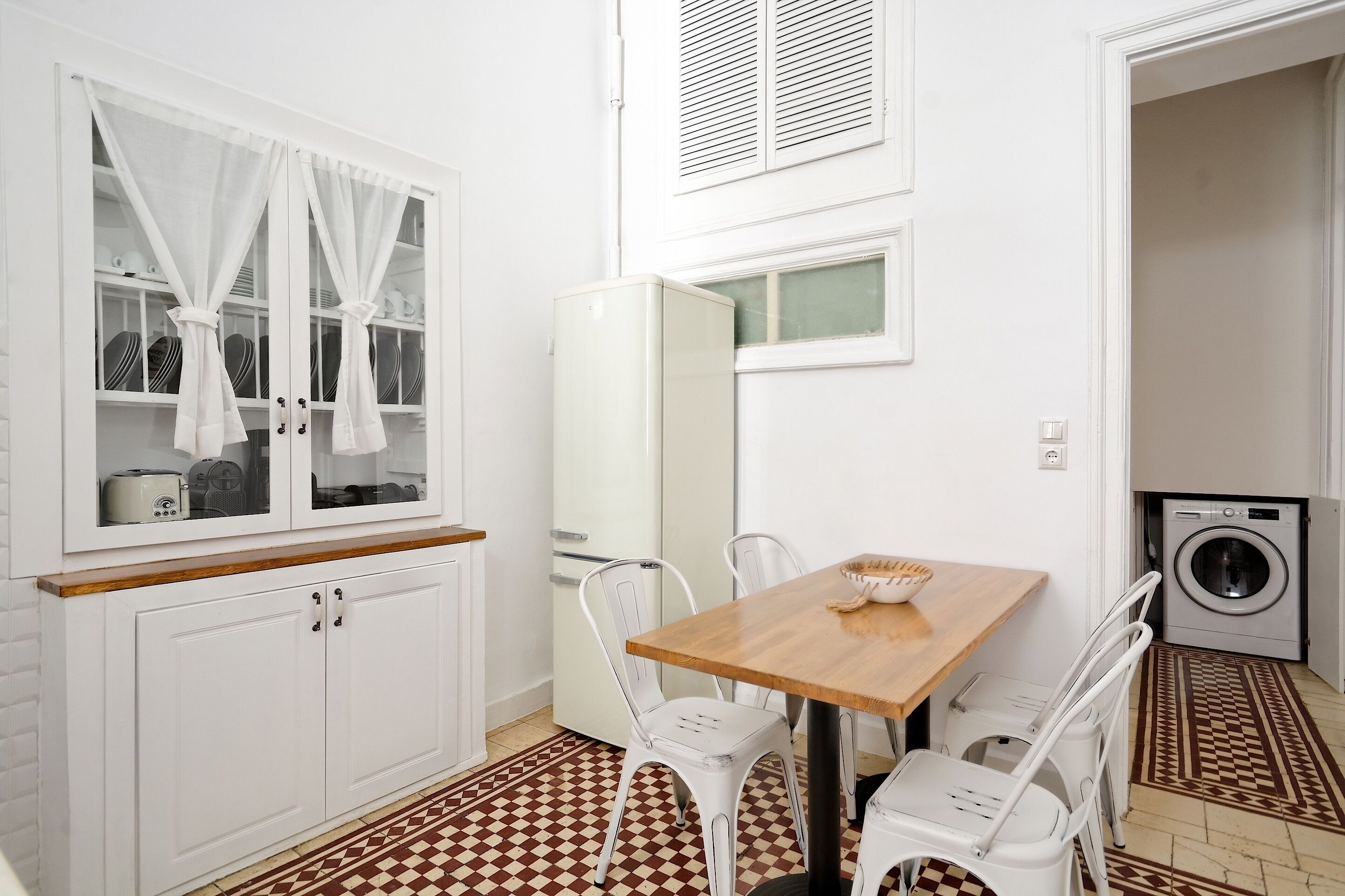 Een kleine keuken met witte kastjes, een houten tafel en een wasmachine.