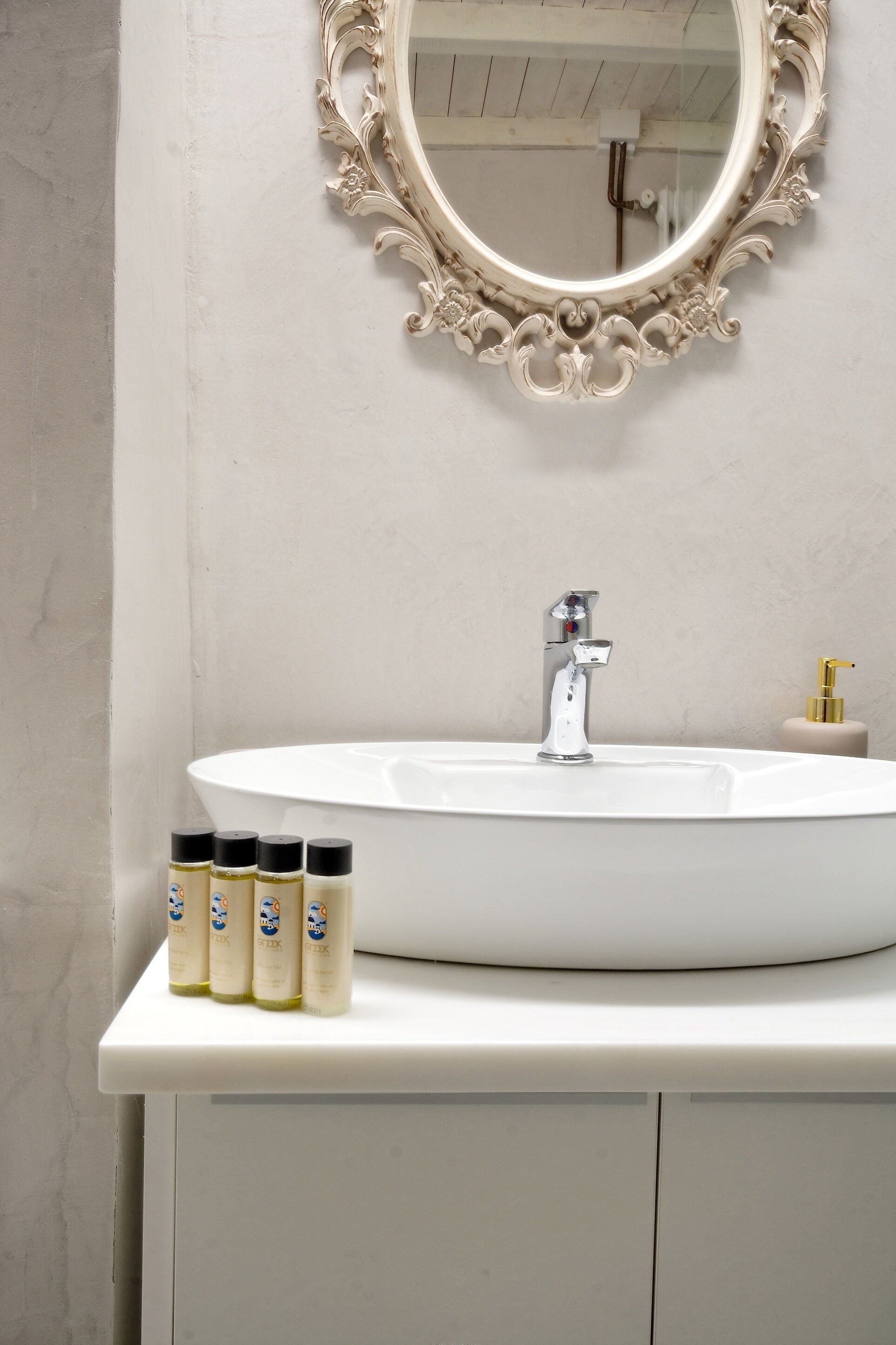 Une salle de bain avec un lavabo blanc, un miroir doté d’un cadre orné et trois flacons de savon liquide posés sur le comptoir.