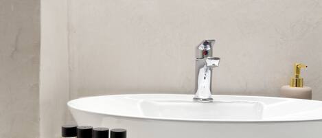 Un baño con un lavamanos blanco, un espejo con un marco decorativo y tres botellas de jabón de manos sobre la encimera.
