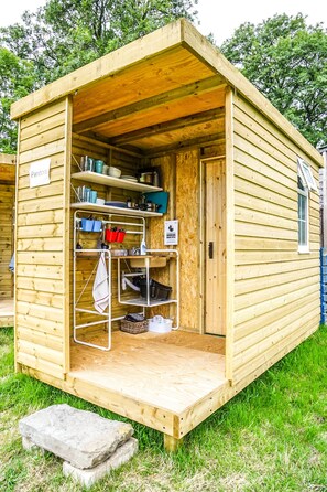 Una cabaña de madera con un pequeño porche, estantes con utensilios de cocina y un letrero que dice 'Pandora'.