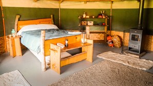 Un dormitorio rústico de madera con cama, mesita de noche, estante con diversos objetos y estufa de leña.