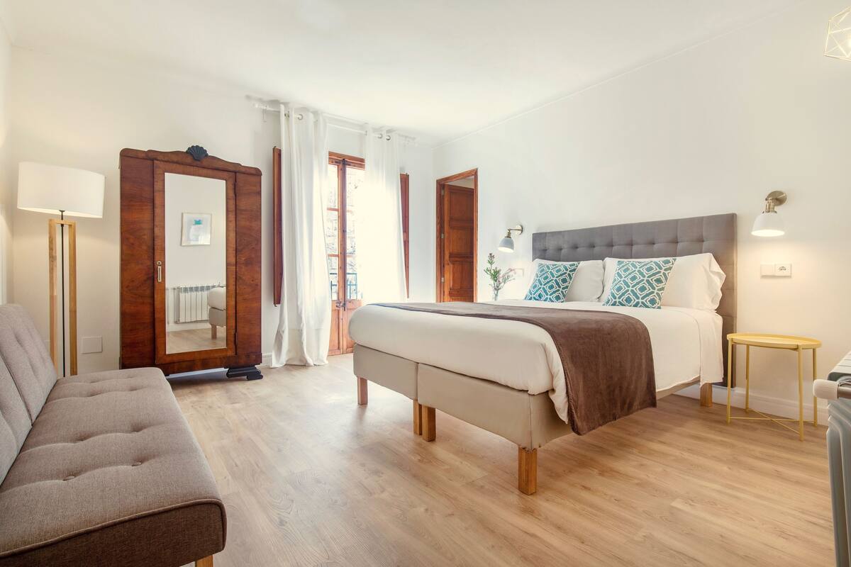 Un dormitorio con cama, mesita de noche, lámpara y sofá.