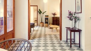 Un suelo a cuadros, vigas de madera en el techo, un sofá, una mesa con jarrones, y un vano que da a otra habitación.