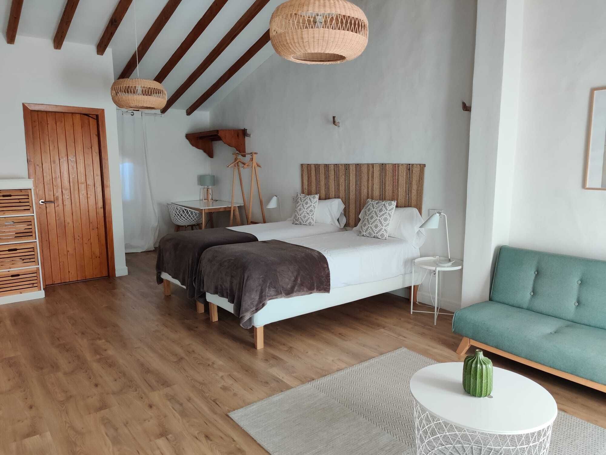 Um quarto espaçoso com uma cama grande, um sofá verde, uma mesa redonda pequena e um guarda-roupa de madeira.
