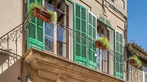 Un edificio con balcón, contraventanas verdes y fachada de piedra.