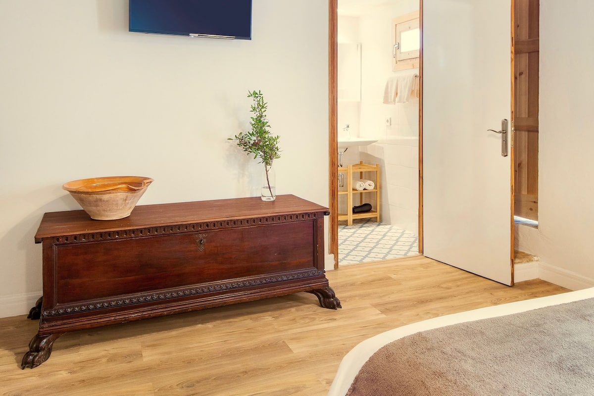 Una habitación con vigas de madera en el techo, un aparador de madera con un cuenco, una planta pequeña y un televisor en la pared.