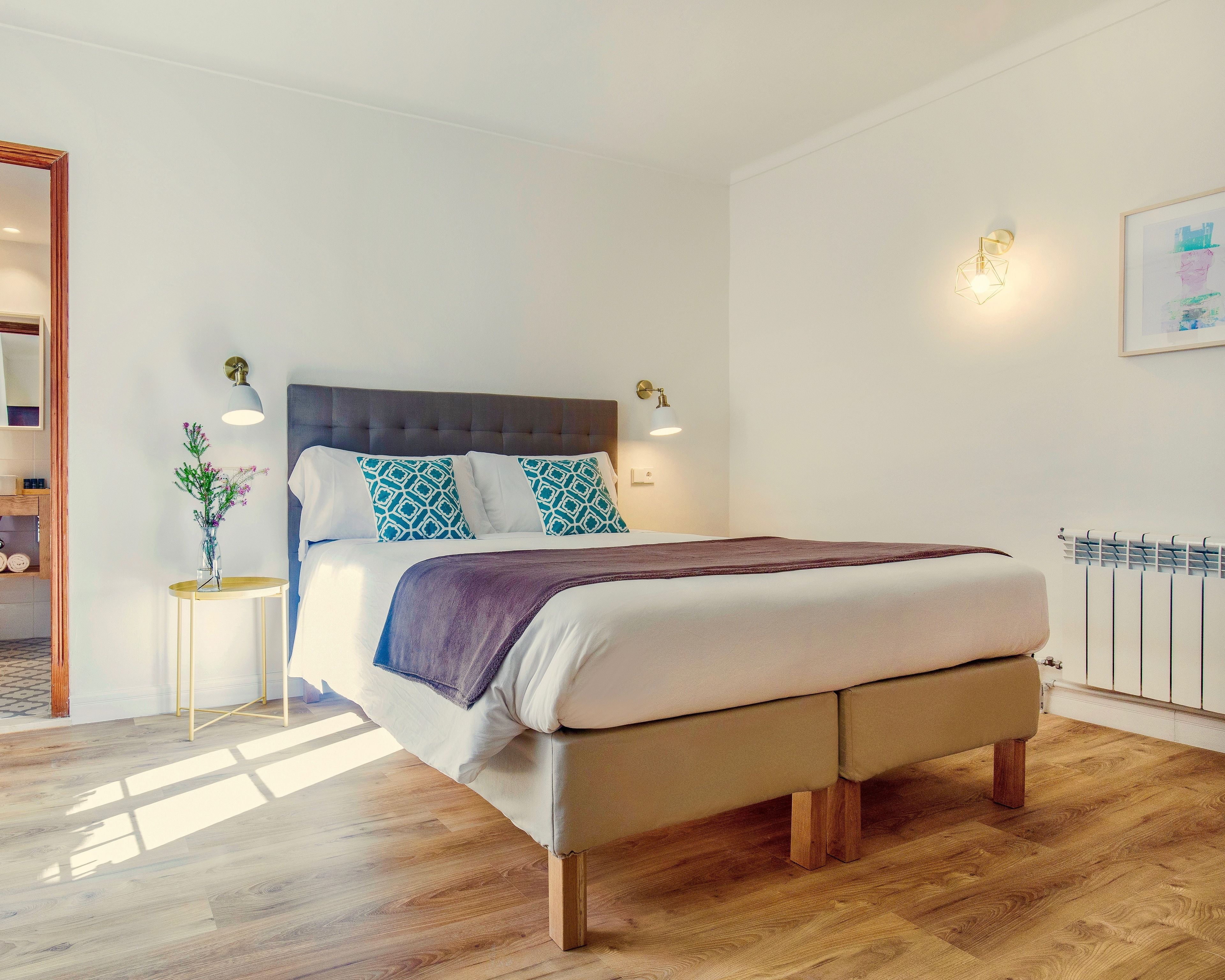 Un dormitorio moderno con una cama grande, una mesita de noche con un florero y una lámpara de pared.