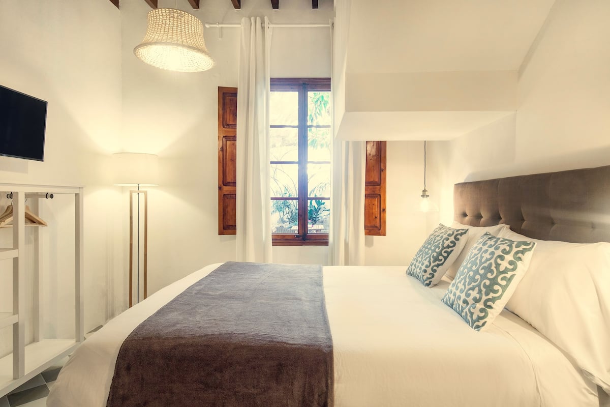Un dormitorio con cama, armario, ventana y una lámpara colgante.