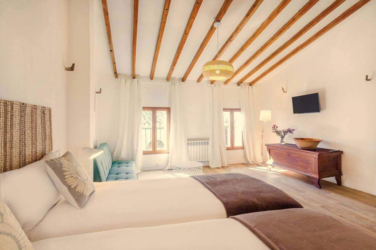 Un dormitorio con una cama grande, una mesita pequeña, un sofá, un televisor y un techo de madera.