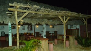 An outdoor seating area with thatched roof, wooden benches, and a tiled floor. - Le Trou Normand (Antsiranana)
