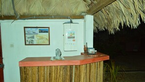 A reception desk with a wooden counter, a thatched roof, and a wall-mounted electrical panel. - Le Trou Normand (Antsiranana)