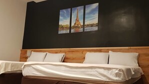 Una camera d'albergo con testiera in legno, un letto con lenzuola bianche e un quadro appeso al muro raffigurante la Torre Eiffel.