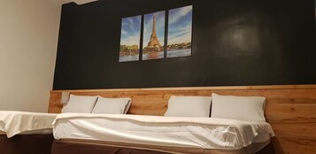 Quarto de hotel com cabeceira de madeira, cama com roupa de cama branca e quadro da Torre Eiffel na parede.