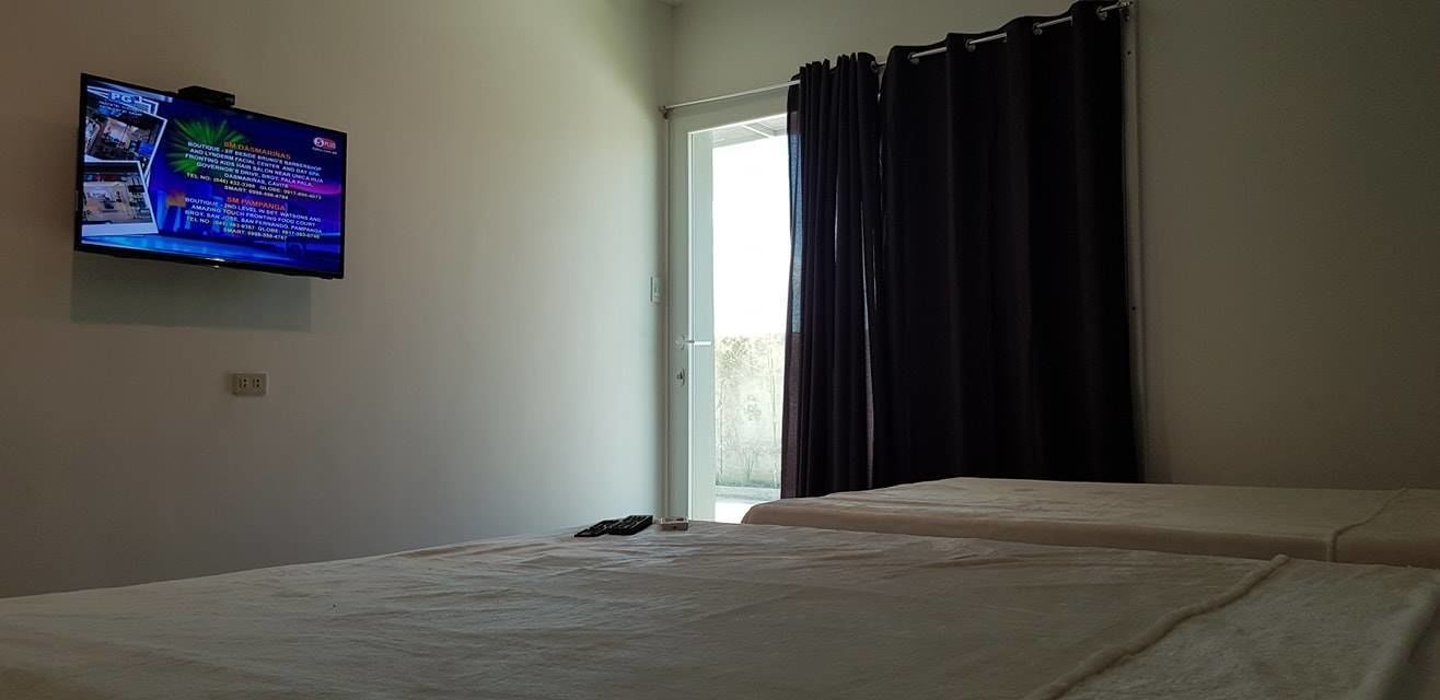 A hotel room with two beds, a television mounted on the wall, and a window with curtains.