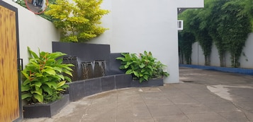 Um pátio com um elemento de água, plantas em vasos e uma porta de madeira.