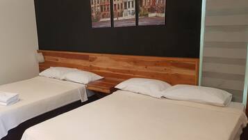 A room with two single beds, wooden headboards, white linens, and a black wall with a street view painting.