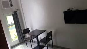 Una stanza con un tavolo, due sedie, una televisione appesa al muro e una finestra con tende.