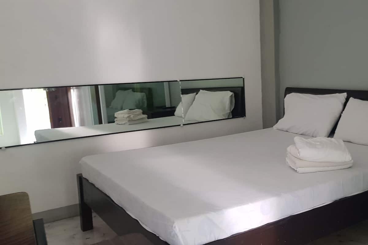 A neatly made bed with white linens and pillows, a small bedside table, and a mirror above the bed.