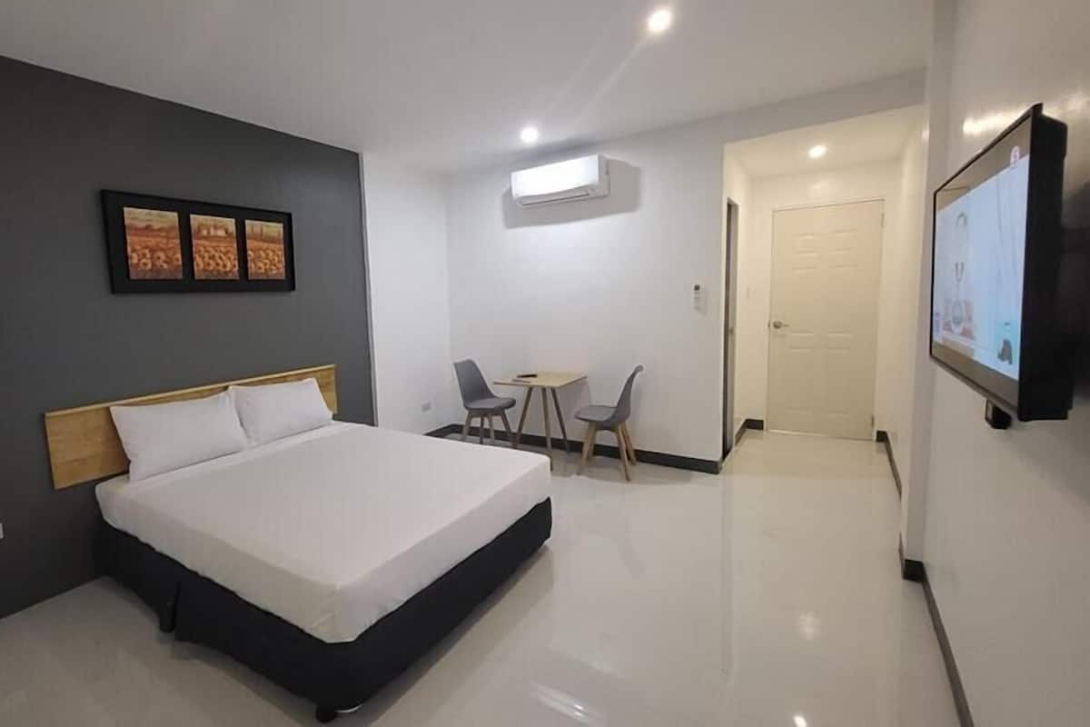 A modern hotel room with a large bed, a small table with two chairs, a TV mounted on the wall, and an air conditioning unit.
