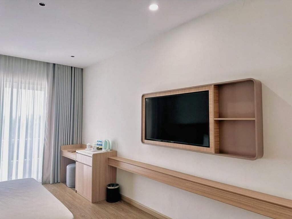 Une chambre d’hôtel moderne équipée d’un lit, d’un bureau avec une chaise, d’un téléviseur fixé au mur et d’une fenêtre avec des rideaux.