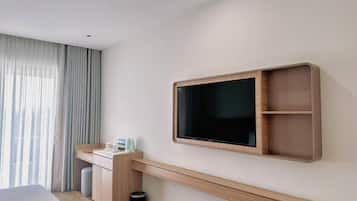 Una habitación de hotel moderna con una cama, un escritorio con silla, un televisor montado en la pared y una ventana con cortinas.