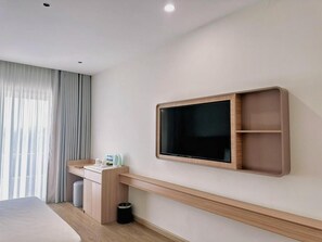 Una habitación de hotel moderna con una cama, un escritorio con silla, un televisor montado en la pared y una ventana con cortinas.