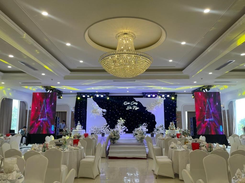 A banquet hall with a stage, white chairs, and a chandelier.