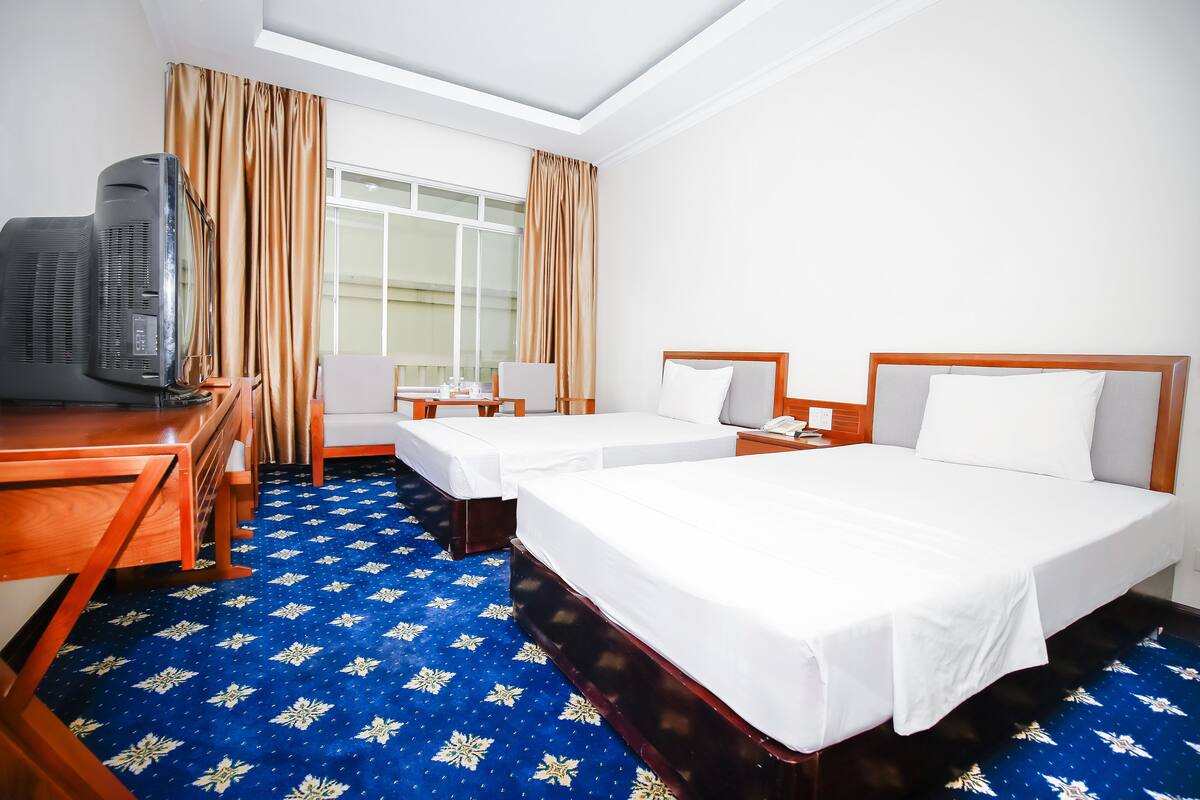 A hotel room with two beds, a desk with a computer, a chair, and an air conditioning unit.