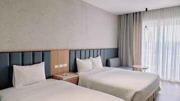 A hotel room with two beds, a headboard, a small table, and a window with curtains.