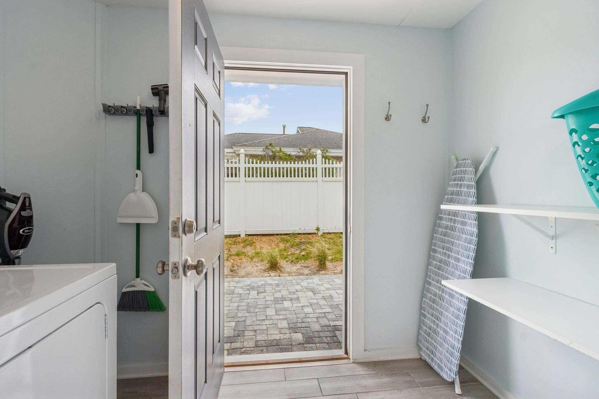 A bathroom with a white door leading to a patio with a white fence and a view of a house.