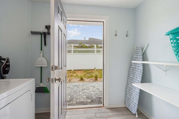 A bathroom with a white door leading to a patio with a white fence and a view of a house.