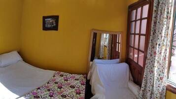 A room with two beds, a wooden wardrobe, a small table, and a window with curtains.