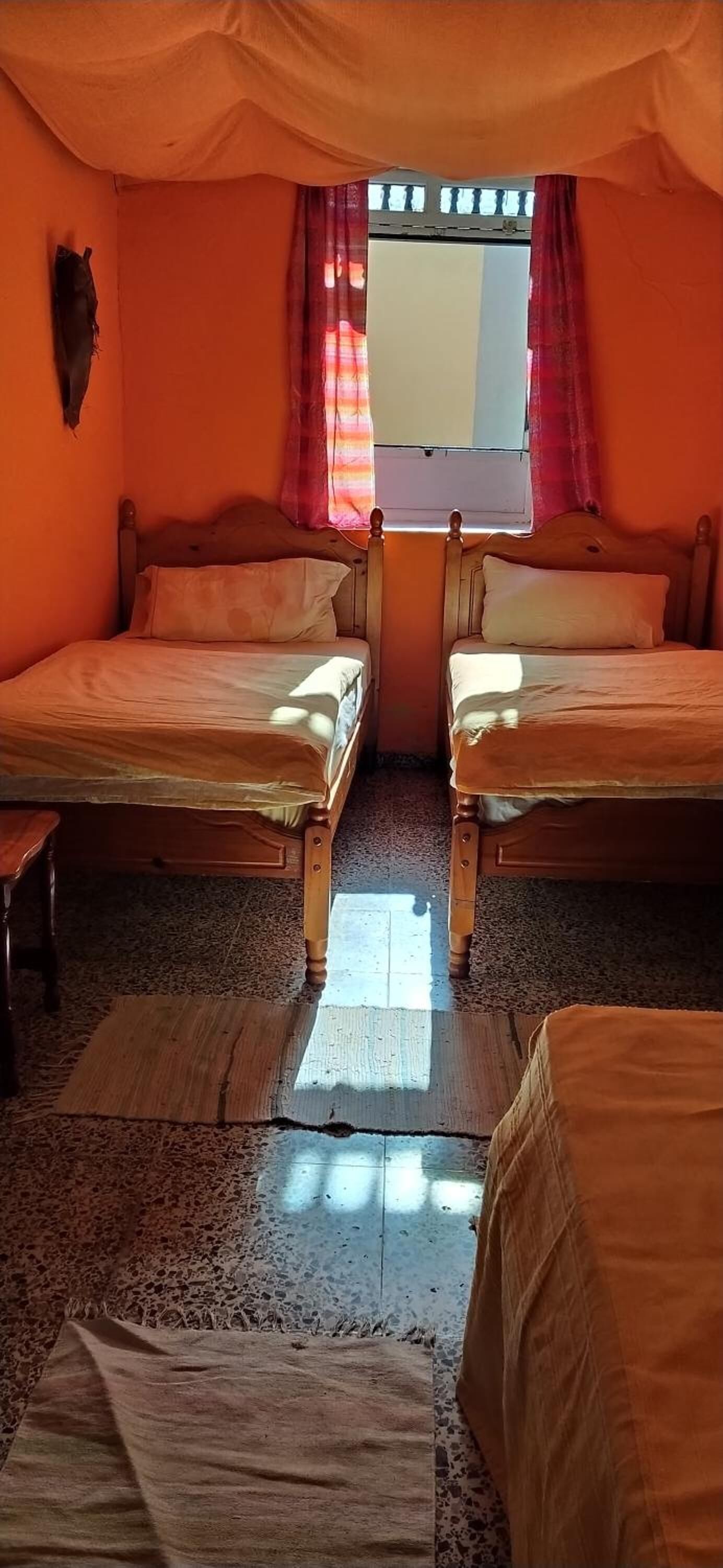 Een kamer met twee houten bedden, een raam met rode gordijnen en een decoratie aan de muur.