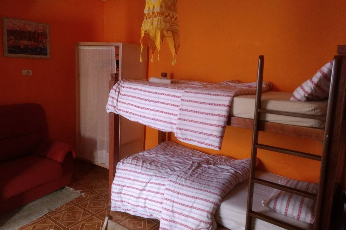 A dormitory room with bunk beds, a red sofa, and a patterned rug.