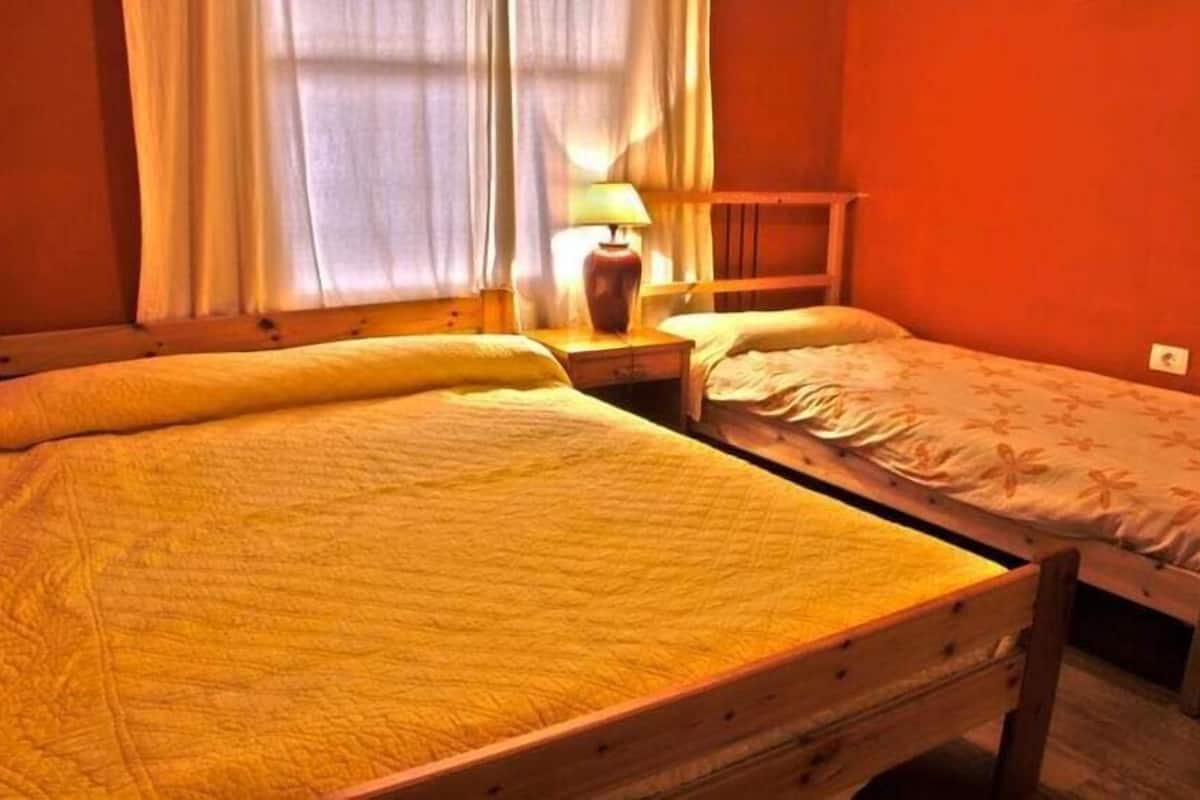 A room with two wooden beds, a nightstand with a lamp, and a window with curtains.