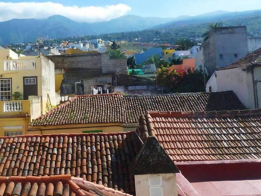 A view of terracotta-tiled rooftops with a distant mountain range and a small body of water in the background.