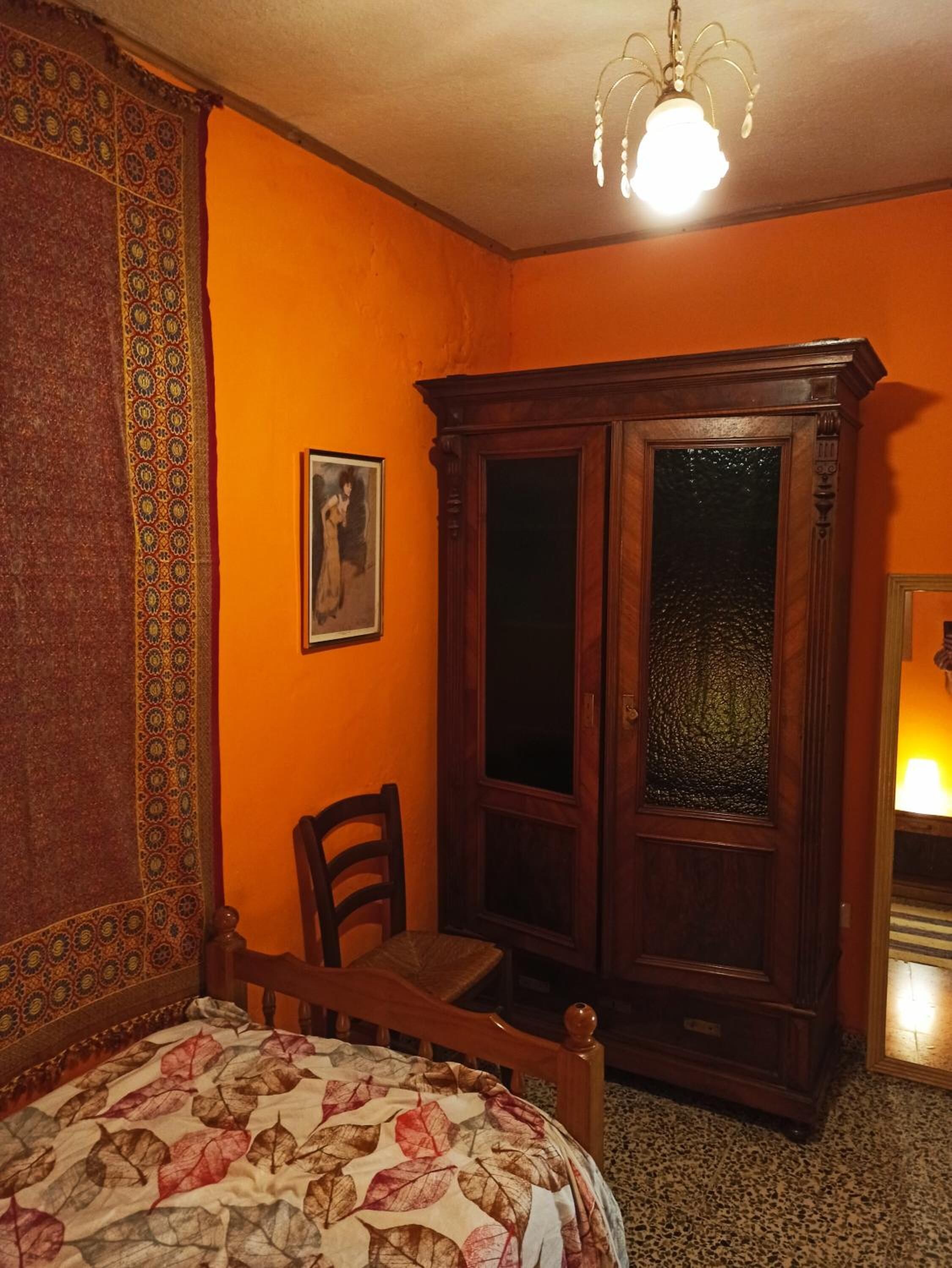 Une chambre à coucher avec un lit, une armoire en bois, une chaise et un tableau accroché au mur.